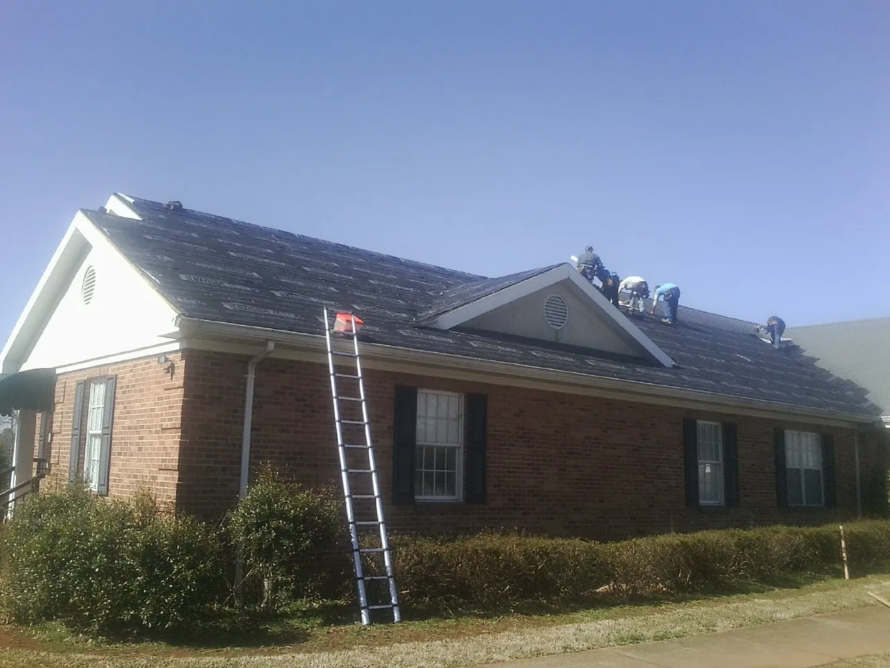 Crew tearing shingles off a brick ranch roof with a ladder set — Metal Roof Repair work by our crew in Pocono Lake