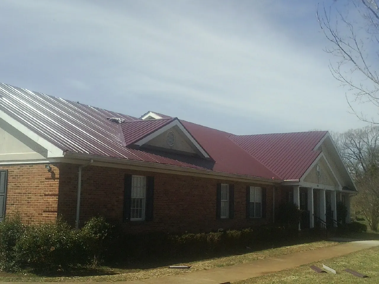 Red metal roof with gabled entries on a long brick building, from a Hail Damage Roof Repair job in Pocono Lake