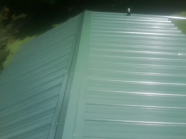 New green metal panels meeting at the ridge of a roof — Flat Roof Repair work by our crew in Pocono Lake