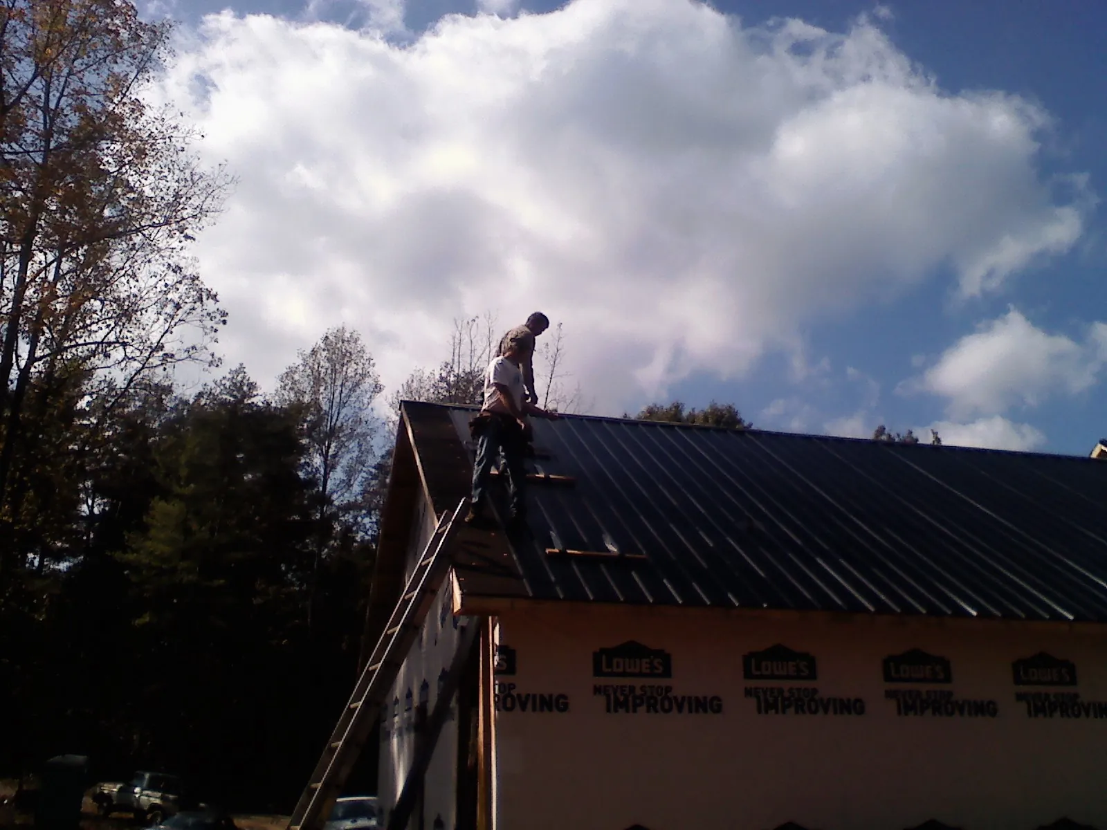 Roofer fastening dark metal panels high against a cloudy sky, from a Roof Inspection job in Pocono Lake