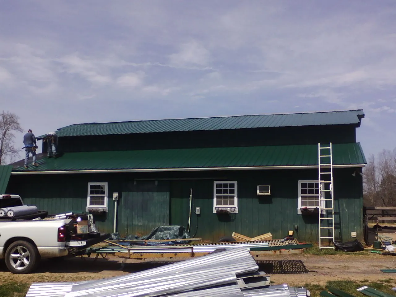 Crew installing green metal roofing on a large green barn in Pocono Lake