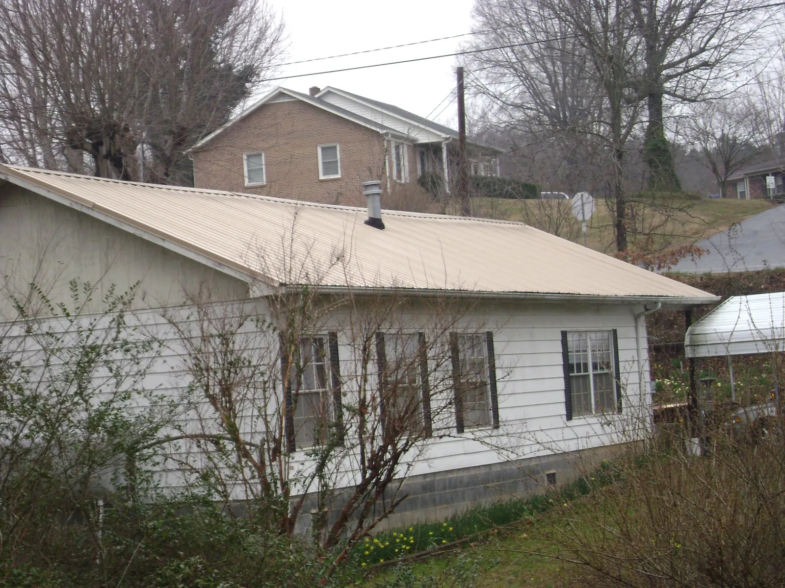 Tan metal roof on a white sided house set into a hillside — Commercial Roofing by Roofing Brothers in Pocono Lake