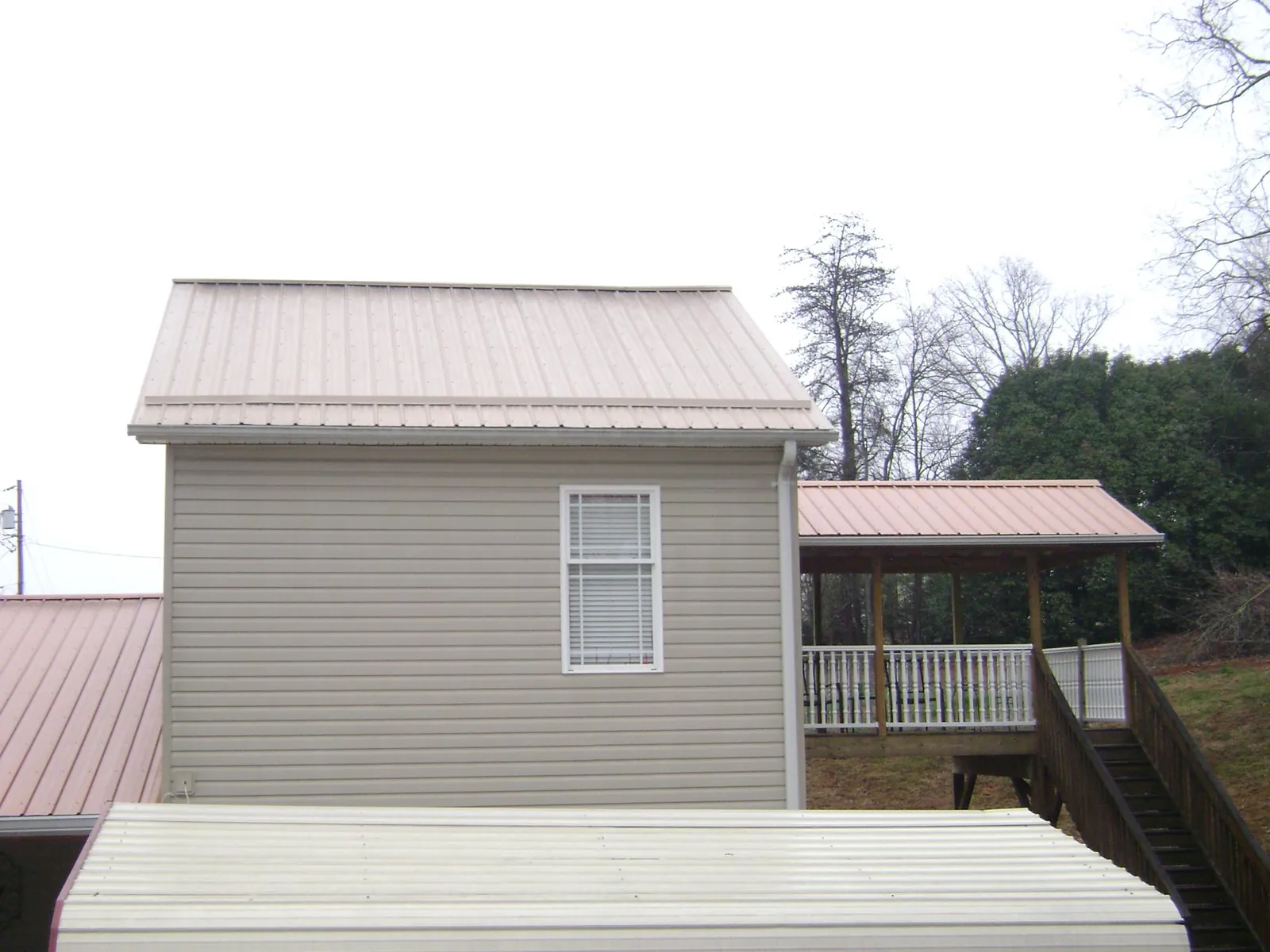 Tan metal roofs on a two story addition and attached porch, from a Roof Replacement job in Pocono Lake